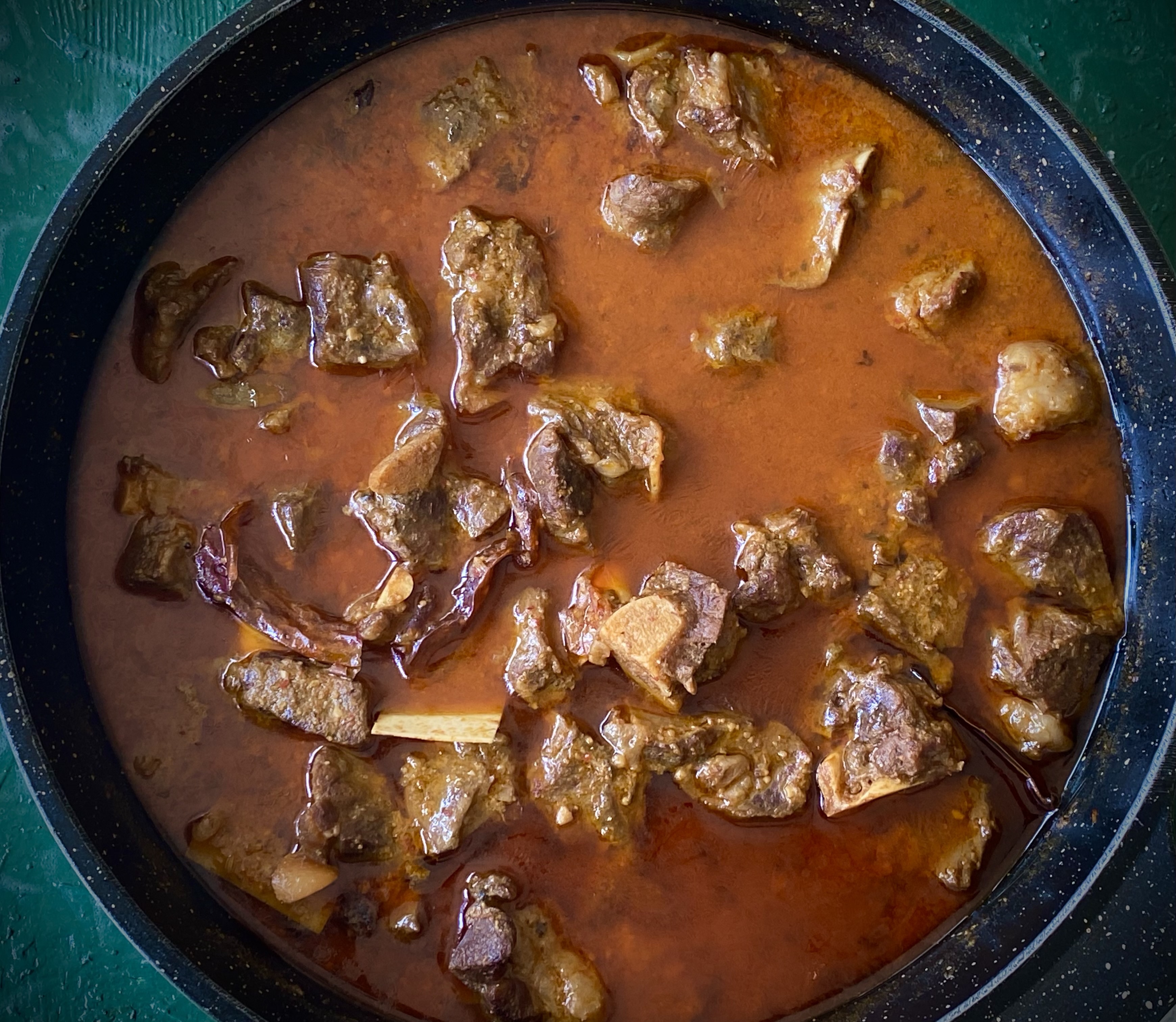 A close-up view of a frying pan filled with pieces of cooked meat in a rich, reddish-brown sauce.