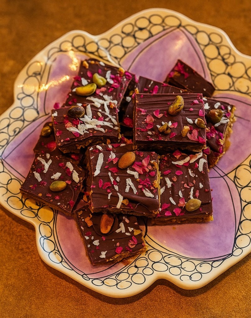 A colorful plate of chocolate bars topped with coconut flakes, pink rose petals, and pumpkin seeds.