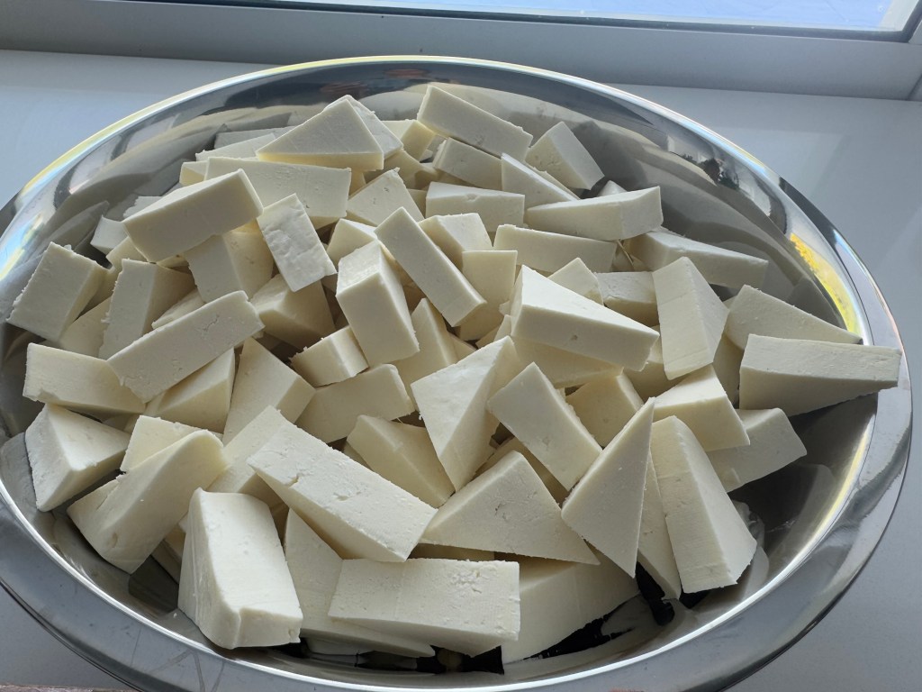 A large, silver bowl filled with neatly cut cubes and triangular pieces of paneer, a type of Indian cheese.