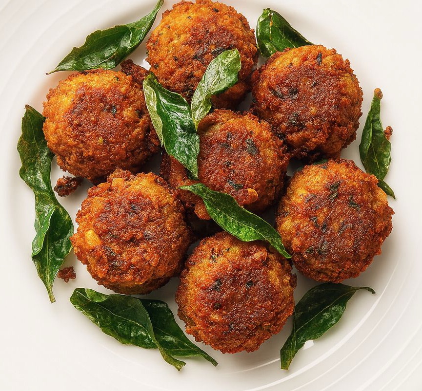 A plate of golden-brown chana dal pakoras garnished with crispy curry leaves, showcasing their round shape and texture.